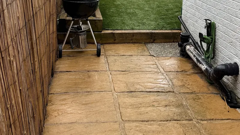 A clean sandstone patio, still wet, beside a lawn