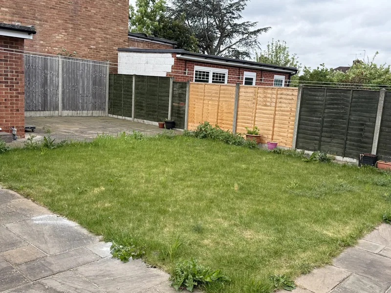 A new lawn beside a paved patio and fence
